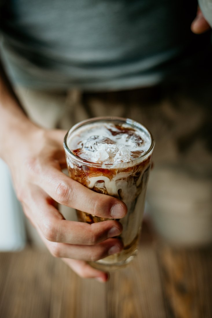 Un hombre preparando un vaso de café con leche helado.